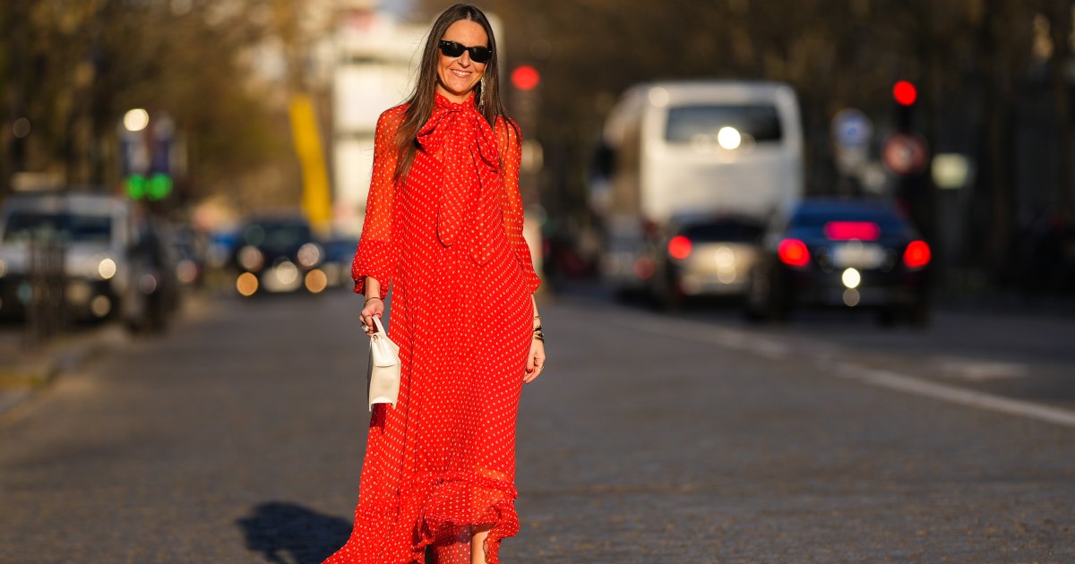 Alba Garavito Torre wears black sunglasses from Ray Ban, gold fringed metallic pendant earrings, a red with beige polka dots print pattern knot high neck / puffy sleeves / ruffled long dress from Zimmermann, gold bracelets, gold rings, a beige matte leather handbag from Jacquemus, gold shiny leather knot toe-cap block heels mules / sandals from What For, during a street style fashion photo session, on March 23, 2022 in Paris, France.
