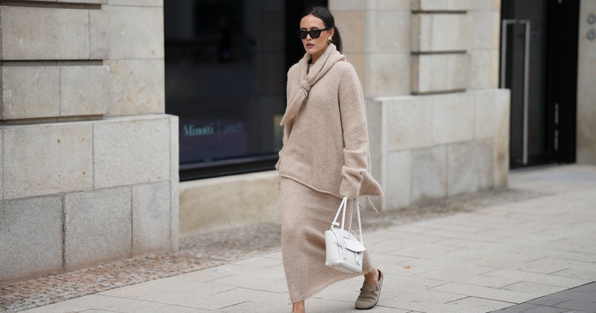 Laura Noltemeyer is seen wearing an oversized beige alpaca wool sweater with tie-back detailing by Aylin König; a long alpaca wool knit skirt in a straight cut by Aylin König; an alpaca knit scarf draped and knotted around the neck by Aylin König; beige suede Boston clogs by Birkenstock; a white intrecciato leather handbag called „Arco Bag“ by Bottega Veneta; slim black cat-eye sunglasses by Yves Saint Laurent; gold statement earrings with a green stone detail by Mango; her brown and straight hair is tied in a low ponytail on October 16, 2025 in Hamburg, Germany.